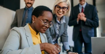 Employee is opening a gift while surrounded by her smiling team.
