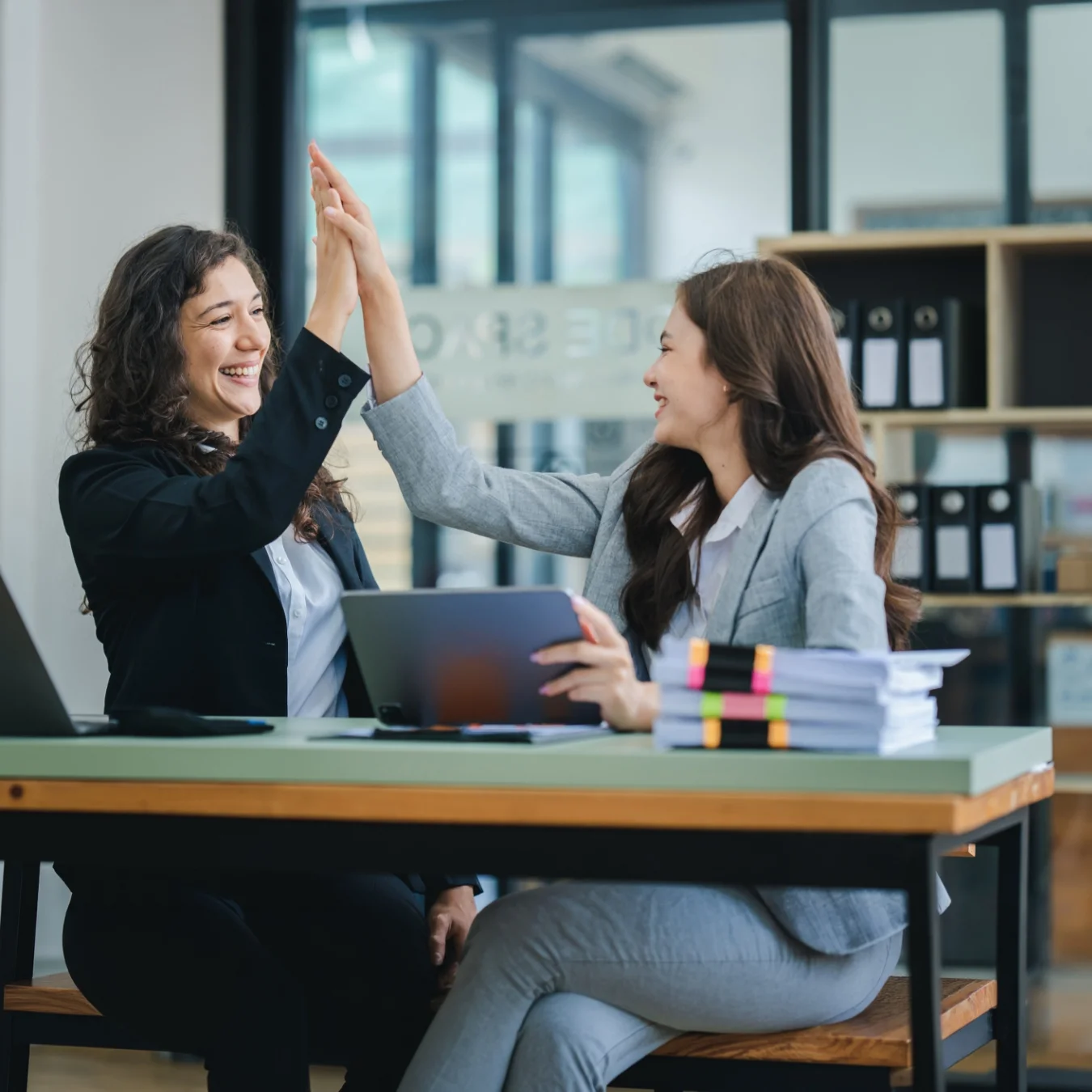 Two co-workers at a desk giving each other a high-five.