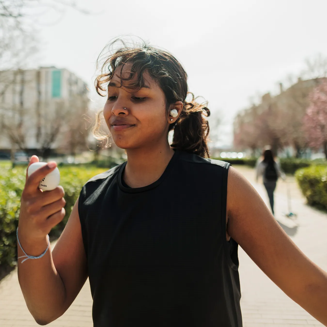 Smiling jogger wearing ear buds in a park is looking at their ear bud charger.