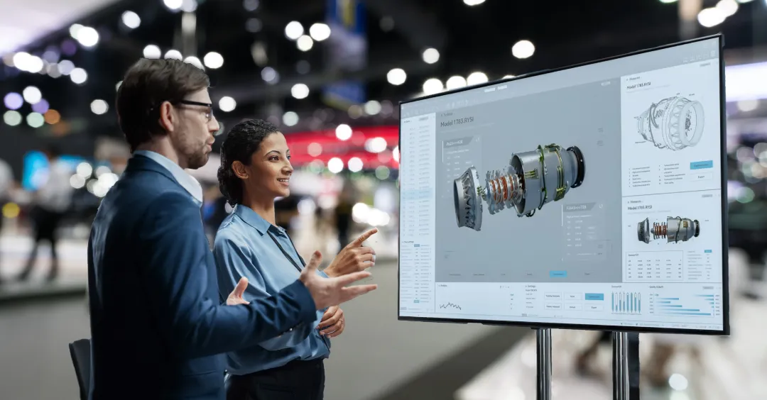 Two people at a trade show standing in front of a product demo screen
