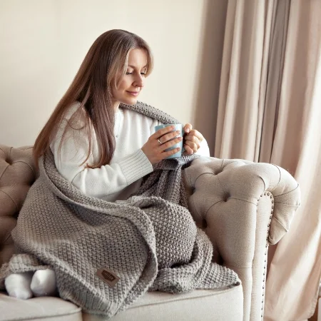 Person drinking from a mug while wrapped in a blanket on a sofa