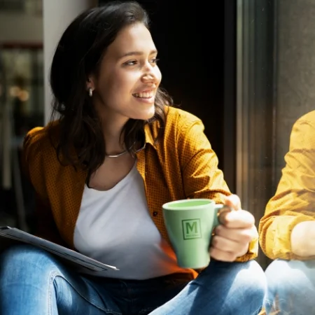 Person is holding a branded mug and looking out a window.