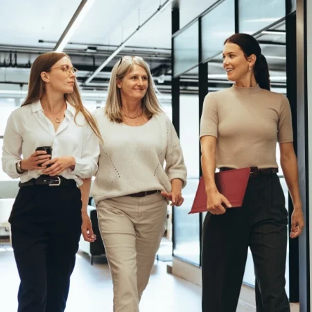 Group of three co-workers smiling and walking in the hallways at work.