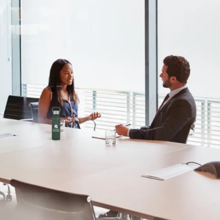 Businessperson interviewing a candidate in a conference room surrounded by glass walls.