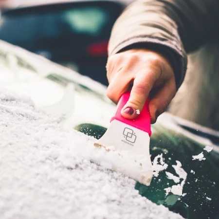 Person using an ice scraper to remove frost from their windshield.