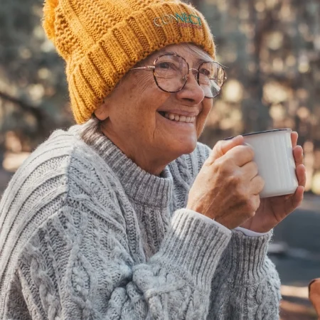 Mature adult wearing a winter hat and holding a mug.