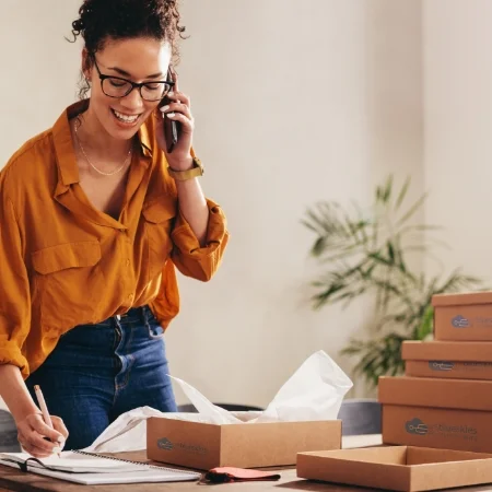 Business owner on the phone. Stacked boxes are on a table next to them.