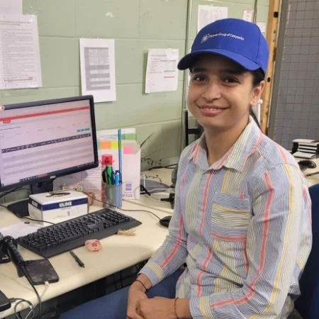 Smiling employee wearing a branded cap and sitting at a desk.