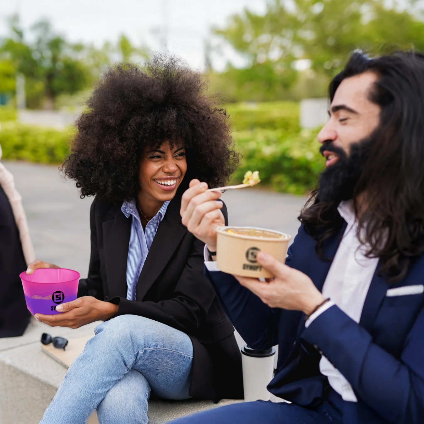 Two co-workers sitting outside laughing and eating lunch.