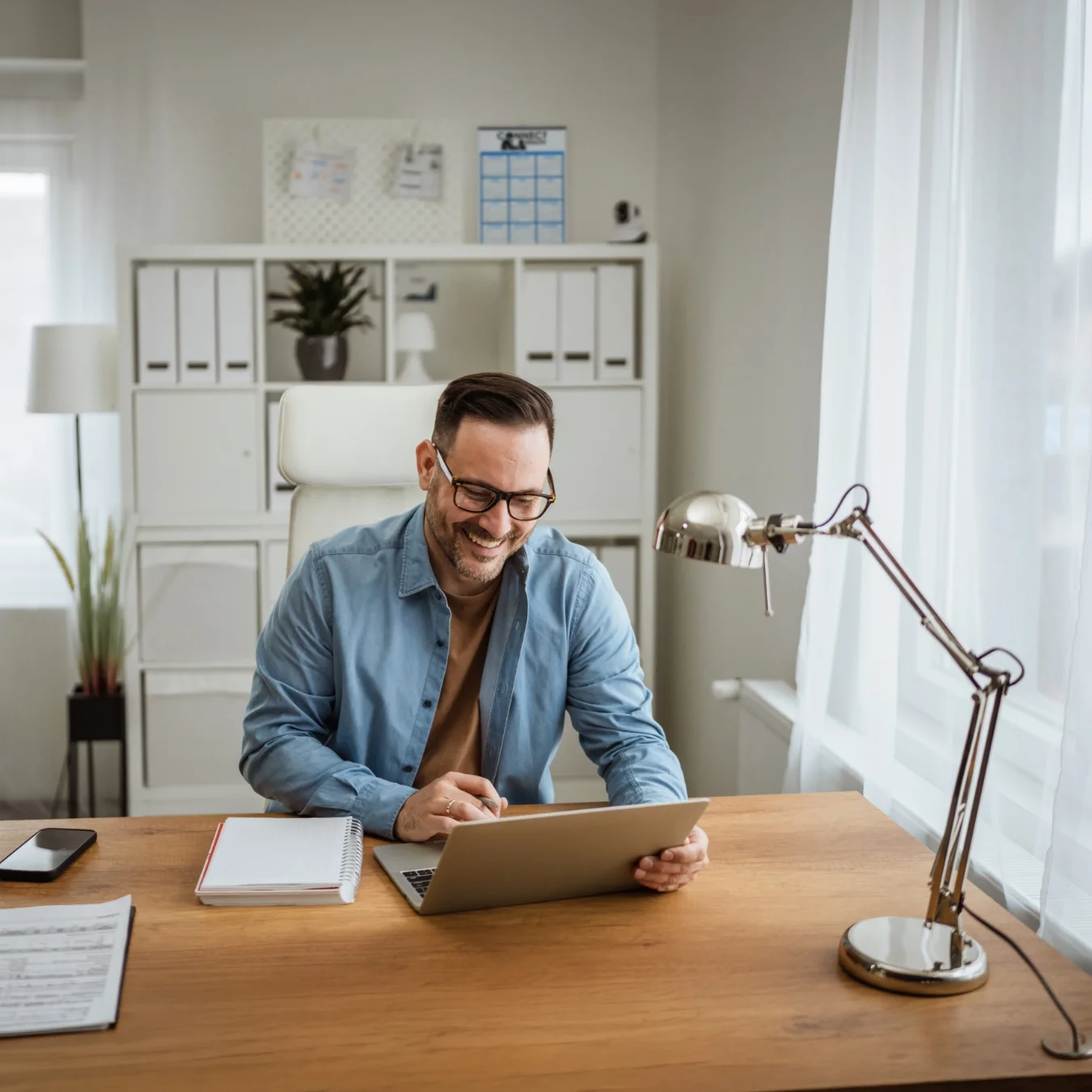 Man wearing glasses while working on his laptop in a home office.