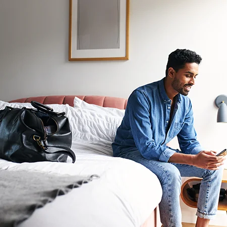 Man sitting on a hotel bed with luggage sitting on the bed