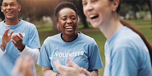 Group of volunteers smiling and clapping together outdoors.