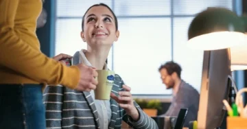 Smiling person being handed a branded mug of coffee from a coworker.