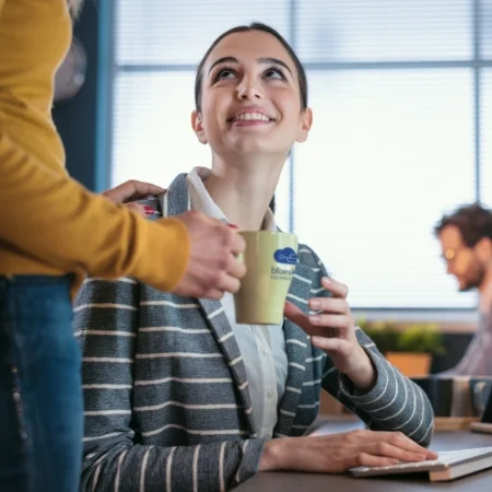 Smiling person being handed a branded mug of coffee from a coworker.