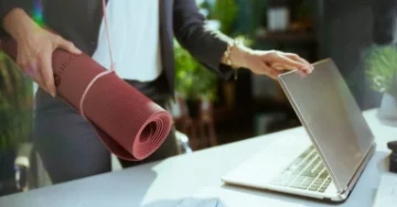 Person at work closing their laptop with a yoga mat slung over their shoulder.