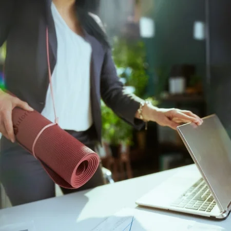 Person at work closing their laptop with a yoga mat slung over their shoulder.