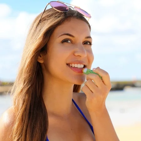 Smiling person with sunglasses on their head applying lip balm.