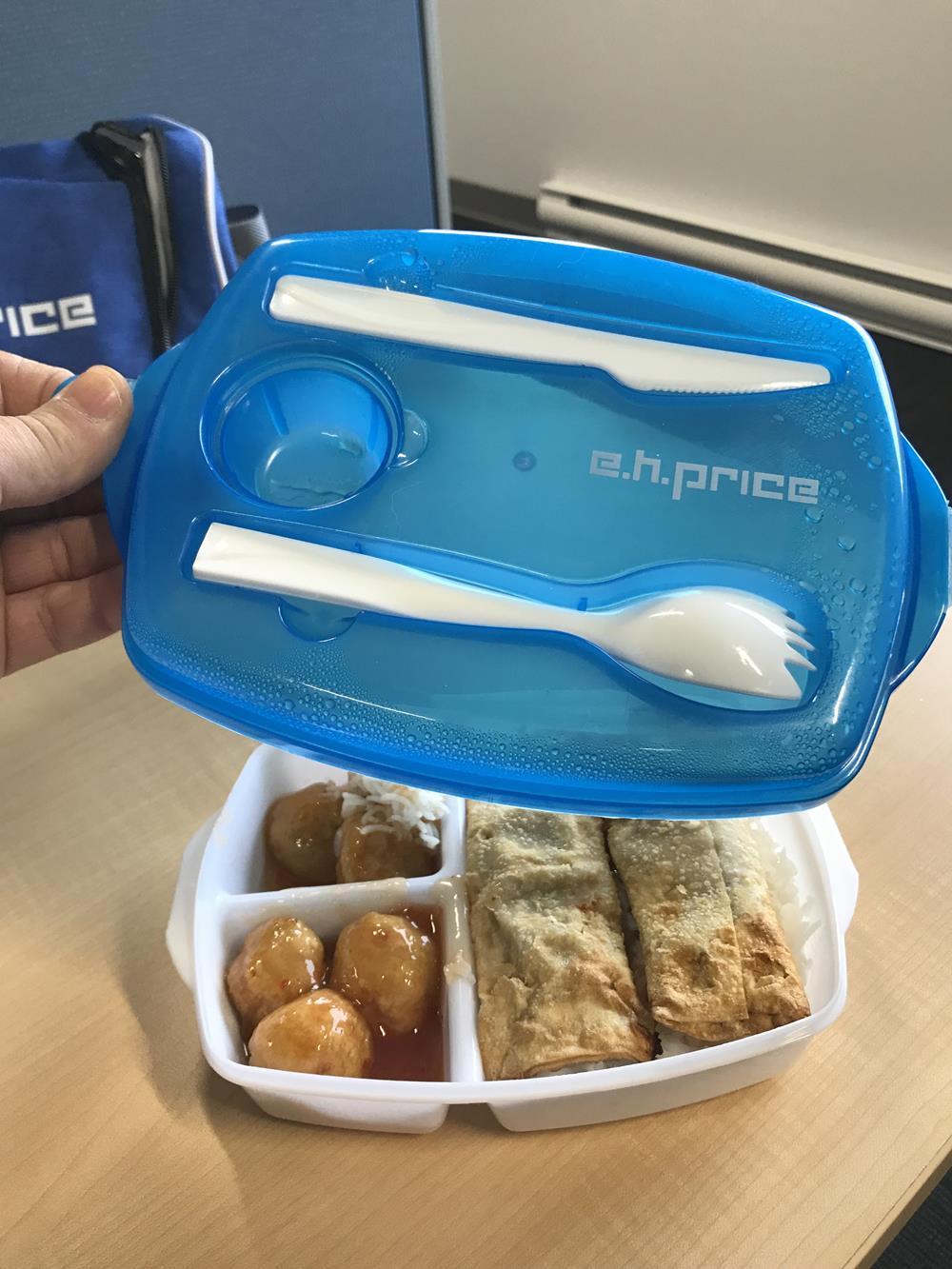 a blue plastic container with spoon and fork over a tray of food