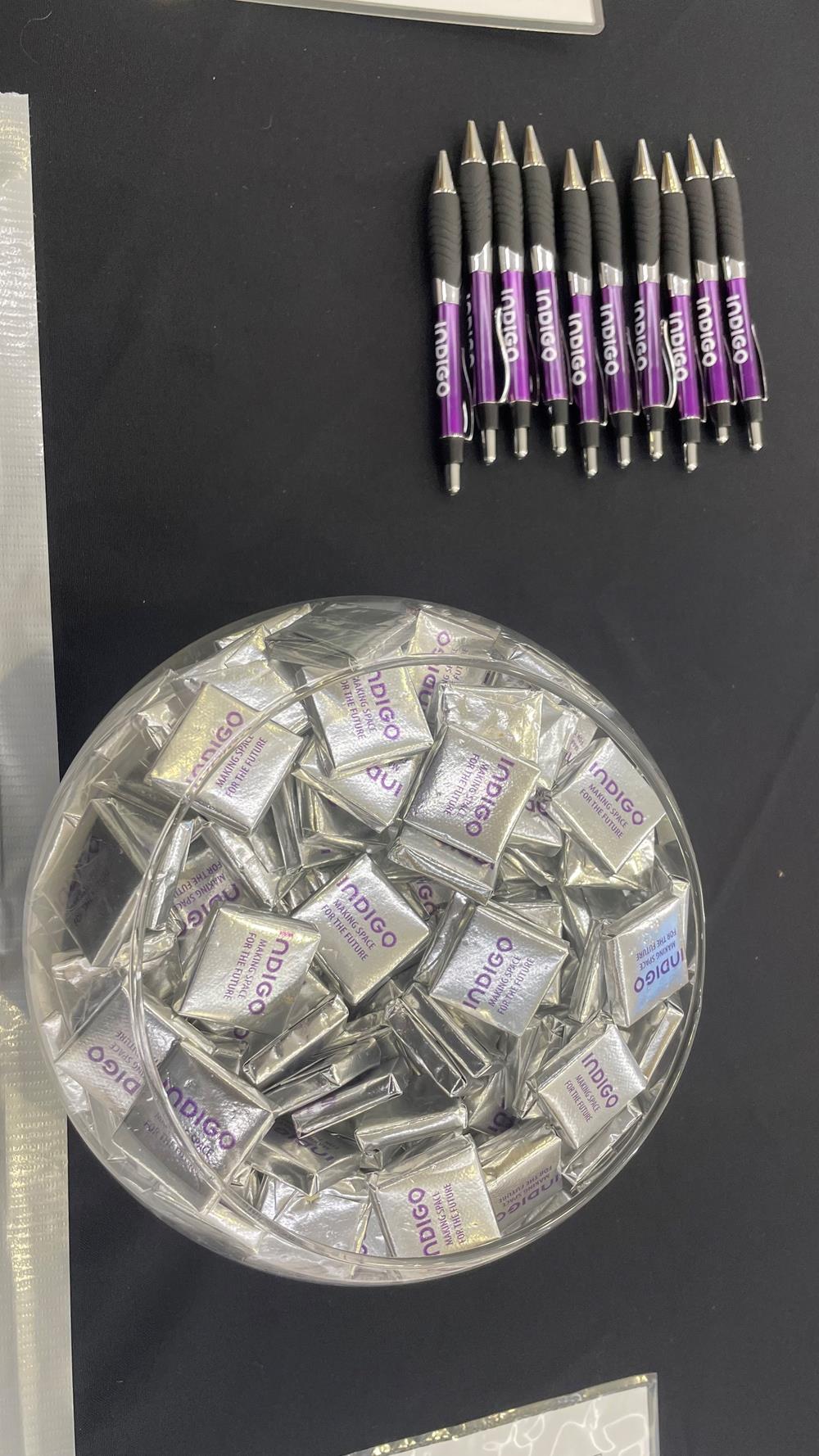 a bowl of candy in a plastic container next to pens