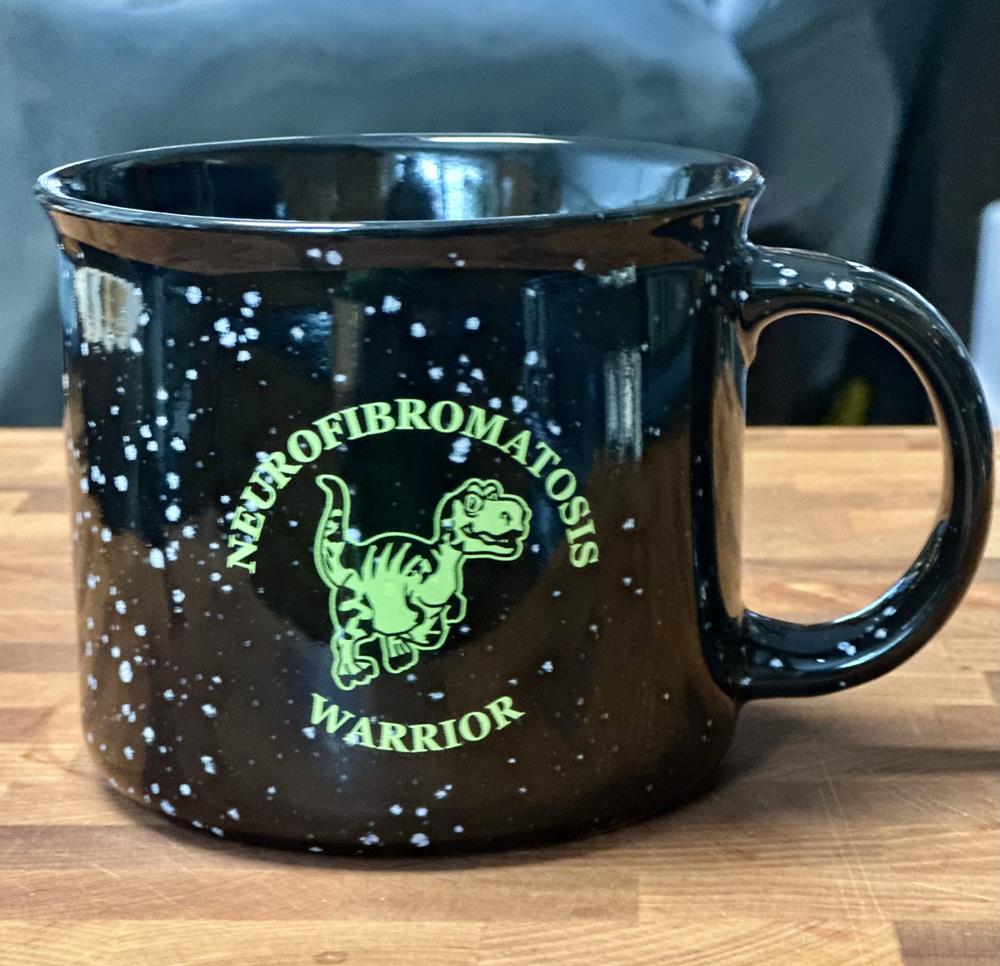 Customer photo from Sue of our Campfire Ceramic Mug - Colours - 15 oz., a black coffee mug with yellow writing on it