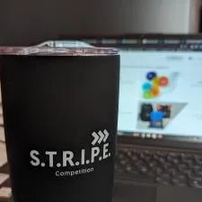 a black cup with a lid on a table in front of a laptop