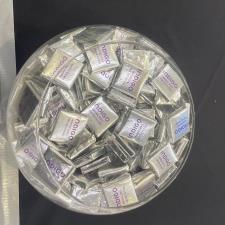 a bowl of candy in a plastic container next to pens