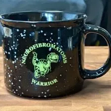 Customer photo from Sue of our Campfire Ceramic Mug - Colours - 15 oz., a black coffee mug with yellow writing on it