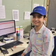 Customer photo from Alex of our Patras Cotton Twill Cap, a woman sitting at a desk with a computer