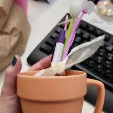 Customer photo from Helena of our Flower Pot Mug - 14 oz., a hand holding a cup with a pen and other objects in the background
